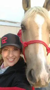 Woman in a black baseball cap takes a selfie with a fawn colored horse