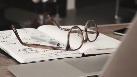 Laptop, notebook and glasses on table