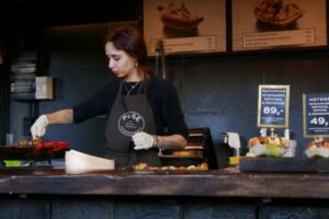 Young woman behind a counter grilling food.