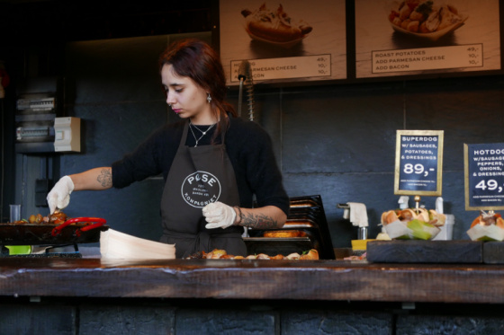 Young woman behind a counter grilling food.