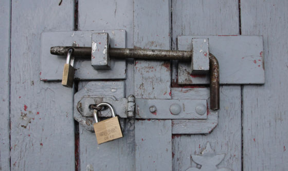 Gray wooden door with bolt and two locked padlocks.