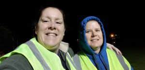Two women in yellow reflective vests take a selfie in the dark