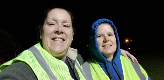 Two women in yellow reflective vests take a selfie in the dark
