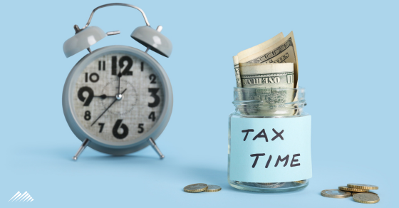 An alarm clock and jar with money in it that reads "tax time"