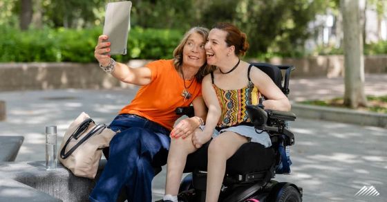 Two women look at a digital tablet. One is in a wheelchair.